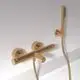 Thermostatarmatur in mattem Goldfinish. Einfache Bedienung durch zwei Griffe. Wandmontage mit Handbrause und flexiblem Schlauch. Ideal Standard Produkt.